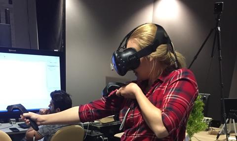 Kate Kapalo is shown from the side, wearing a black headset and holding black controllers.
