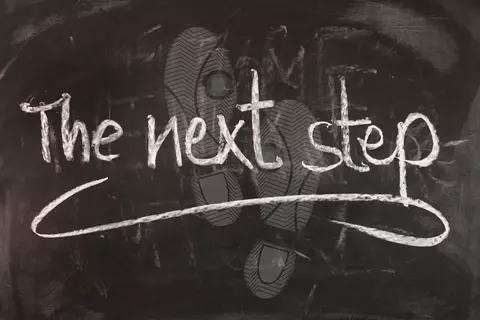 Footprints with "the next step" written on top in chalk.