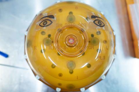 A spherical device encased in yellowish plastic has eyes drawn on the top. 