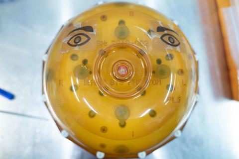 A spherical device encased in yellowish plastic has eyes drawn on the top.