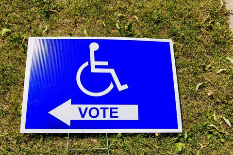 A polling station sign depicts an icon of a person in a wheelchair above the word "vote."
