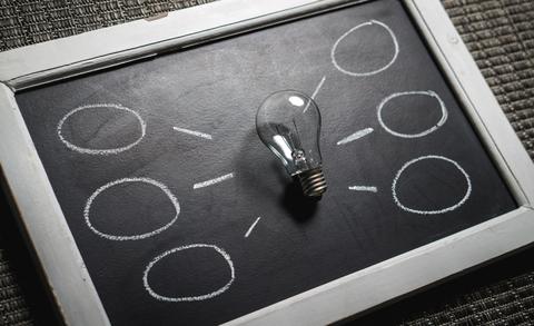 A lightbulb placed on a blackboard with circles drawn in white chalk around the lightbulb