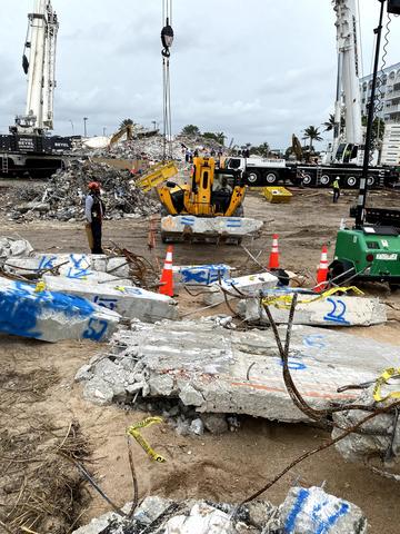 Pieces of concrete marked with blue spray paint lay on the ground amid pieces of construction equipment. 