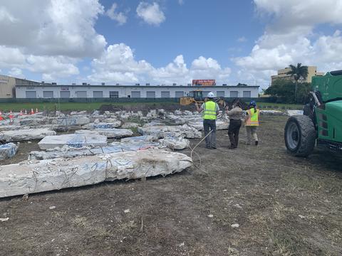 Broken pieces of concrete marked with blue spray paint lay on the ground near a storage facility. 