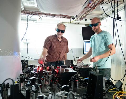 Two men in dark goggles stand over a table of scientific equipment.