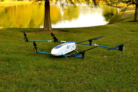 A six-propeller drone sitting on the grass in front of a lake