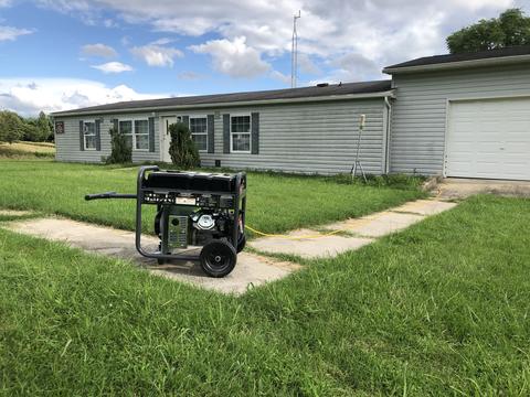 A portable generator is placed on the sidewalk far away from a home. 