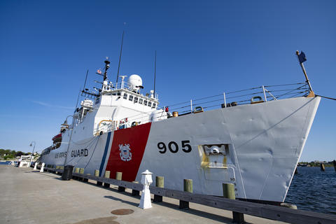 A white and red ship marked U.S. Coast Guard is tied up along a concrete dock. 