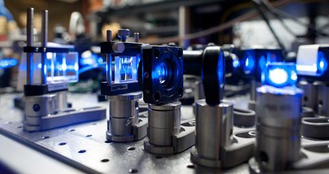 Lenses on short stands are lined up on a lab table with blue light shining through them.