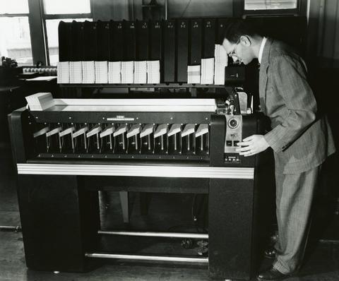 A man bends over the end of a table-sized machine with a row of sorting mechanisms.
