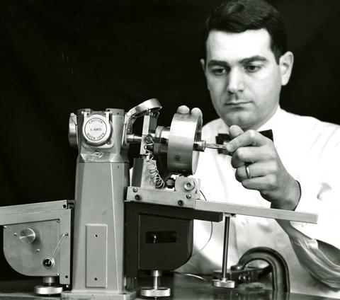 A man turns a part on a tabletop scientific device in a historical photo.