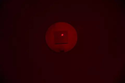 A square chip with a red laser dot lies on a round metal disk in a darkened space. 