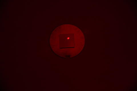 A square chip with a red laser dot lies on a round metal disk in a darkened space. 