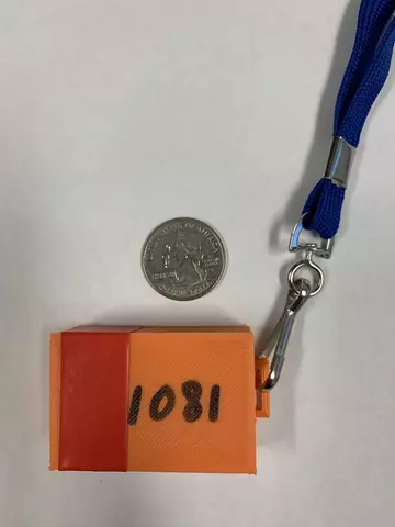 A numbered orange plastic box on a lanyard is shown with a quarter for scale.