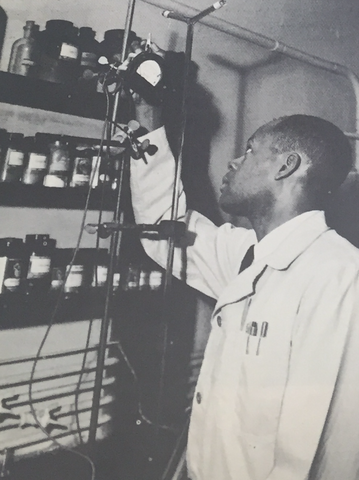 John Sligh, wearing a lab coat, reaches up to adjust a piece of equipment.