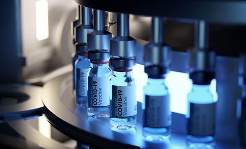 Vials labeled "COVID-19 Vaccine" are being filled on a machine. 