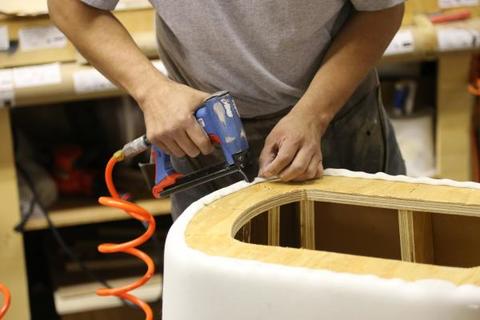 A person is using a tool to attach foam to wood for upholstered furniture.