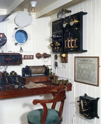 A small room features a wooden desk, a porthole, and historical telegraph equipment on the walls.