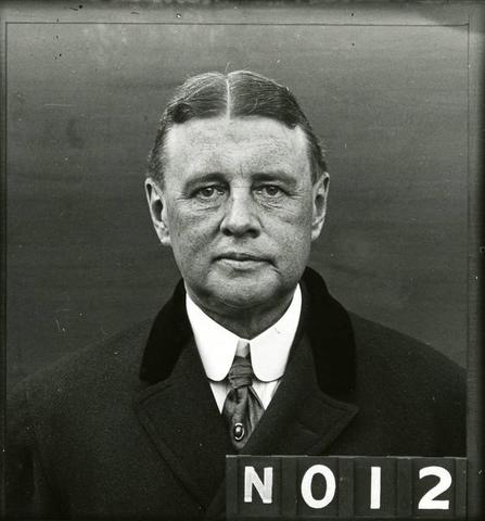 black and white headshot of a man in a suit and tie. The code N012 is in the bottom right corner.