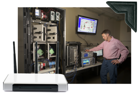 In main photo, a man stands near a counter holding electronic equipment. Photo of router is overlaid in lower left.