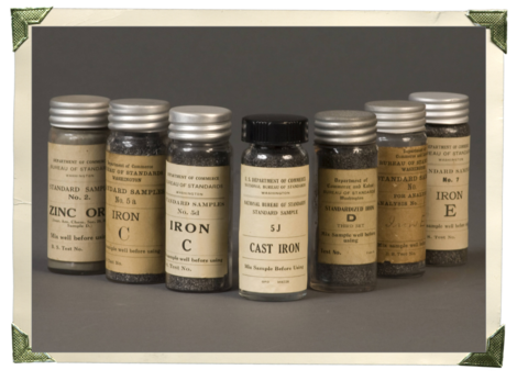 Seven glass bottles with old-fashioned labels include reference materials for cast iron and zinc ore.