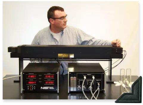 A man wearing safety glasses stands in front of a wide black device, the Standard Reference Photometer. 