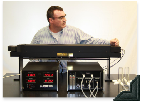 A man wearing safety glasses stands in front of a wide black device, the Standard Reference Photometer. 