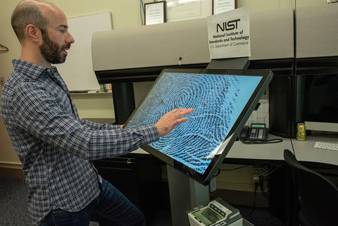 Greg Fiumara, in an office setting, looks at a large screen showing a close-up fingerprint.