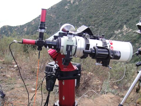 A white telescope on a red stand is outdoors with mountains in the background. 