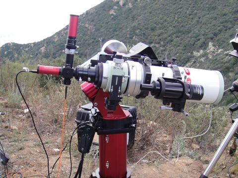A white telescope on a red stand is outdoors with mountains in the background.