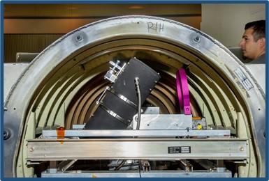 A man stands to the right of an arch of metal with a telescope and other equipment inside.