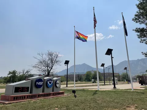 Entrance signs for NIST and NOAA are in the left foreground, with flagpoles, mountains and blue sky in the background.
