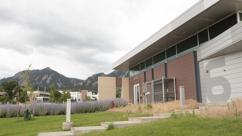 A low modern building at right has a large "6" on the side, with mountains and cloudy sky in the background.