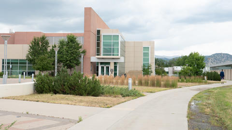 Angular office building in the center, with a sidewalk in front leading to the right and mountains in the background.