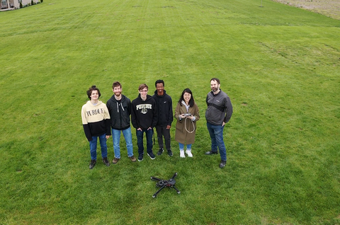 Photo of Purdue University team members standing in grass field with drone