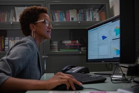 Side view of Danielle Brager at a desk, looking at a monitor, hand on a computer mouse.