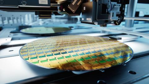 A circular silicon wafer lies flat under manufacturing equipment at a factory. 