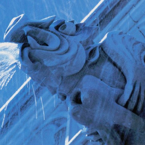 View from below of stone gargoyle spitting water and holding a large molar tooth. 