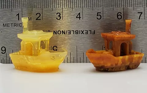Two miniature tugboat replicas sit in front of a metal ruler. 