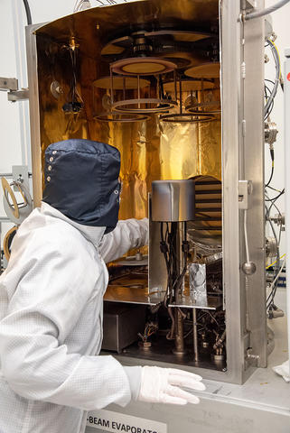 A researcher wearing coveralls reaches into a tall open piece of scientific equipment lined with aluminum foil. 
