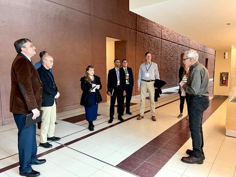 Interior hallway of a building. Man on right stands looking at a group of individuals on the left.