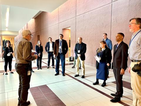 Interior building hallway. Man on left speaks to a group of people on the right.