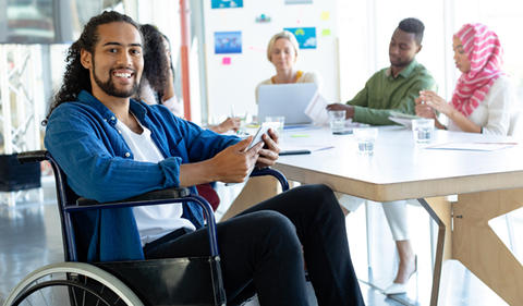 Man in a wheelchair working at a table with diverse co-workers