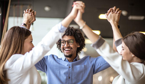 Three co-workers holding hands above their heads feeling empowered.