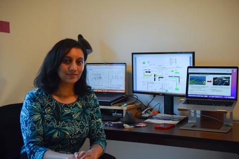 Nehika Mathur sits at a workstation with multiple computer monitors.