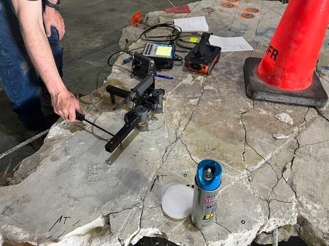 A worker uses a specialized device to tap on a large piece of broken concrete. 