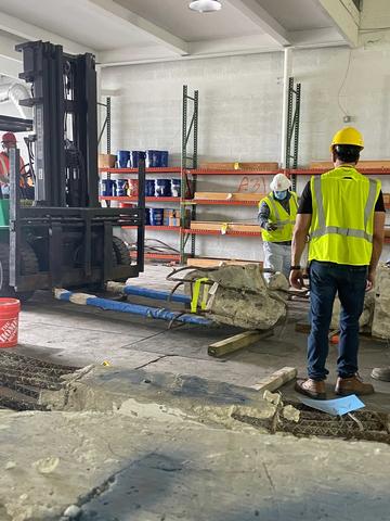 Two people in hard hats and safety gear stand looking at a large piece of concrete on a forklift. 