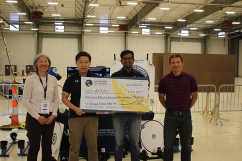 Three men and one woman at a drone competition. Two of the men are holding up a big check to indicate they won the grand prize.