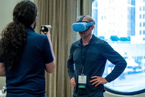  A researcher helps a 5x5 attendee try out a virtual reality headset.