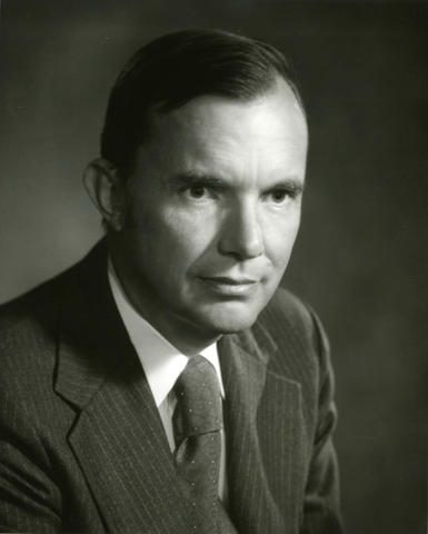 Black and white headshot-style portrait of a man in a suit.